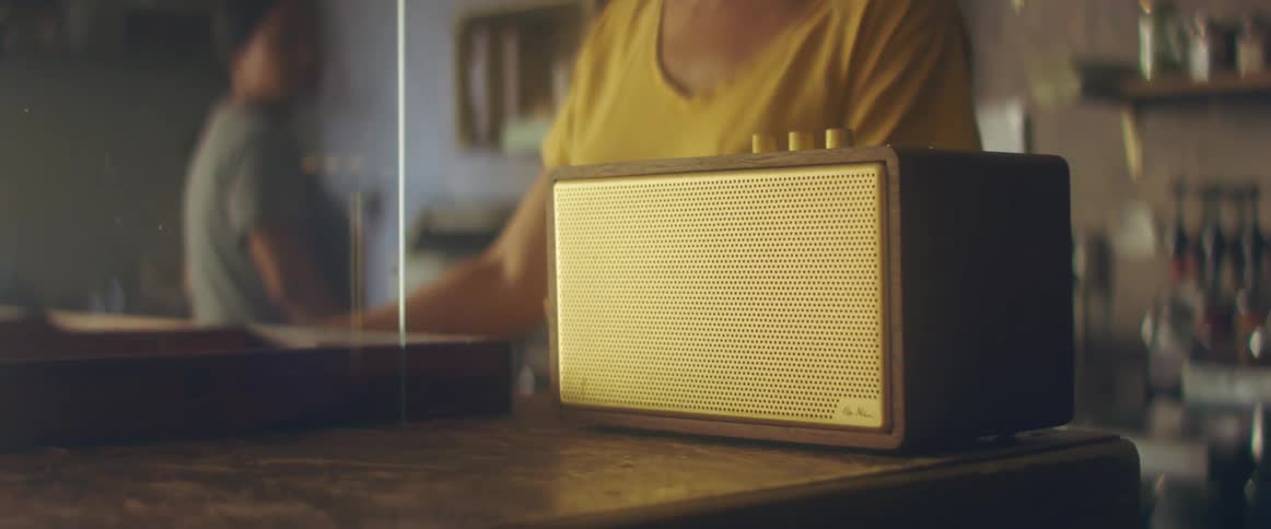 A woman turns a knob atop an old fashioned radio on a counter indoors during the day
