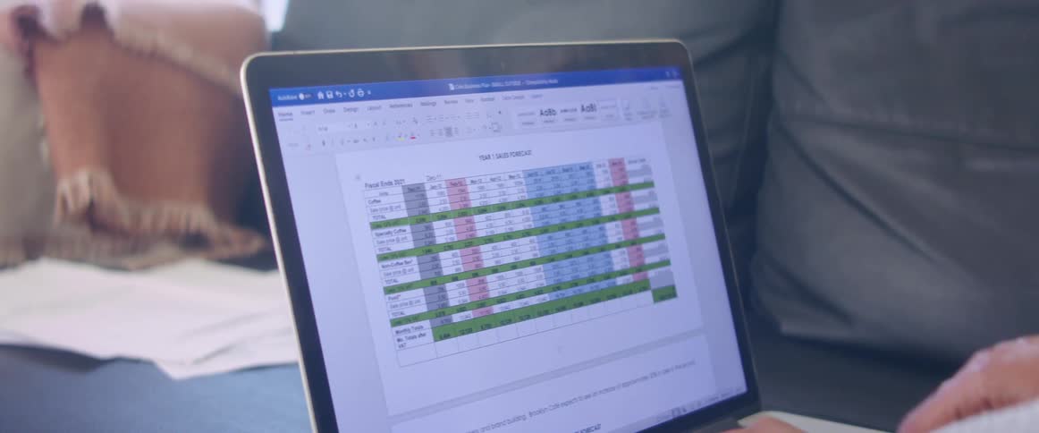 Hands tap and type on a laptop keyboard working on a color coded chart on the sofa