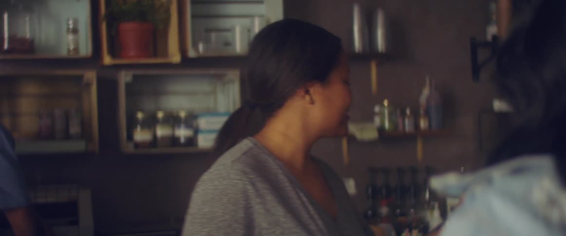 A coffeehouse employee chats with a customer and hands her a drink in a to go cup