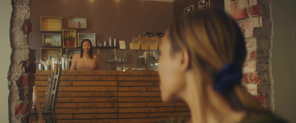 A woman pauses at a cafe doorway looks back at the barista nods and then walks forward with commitment