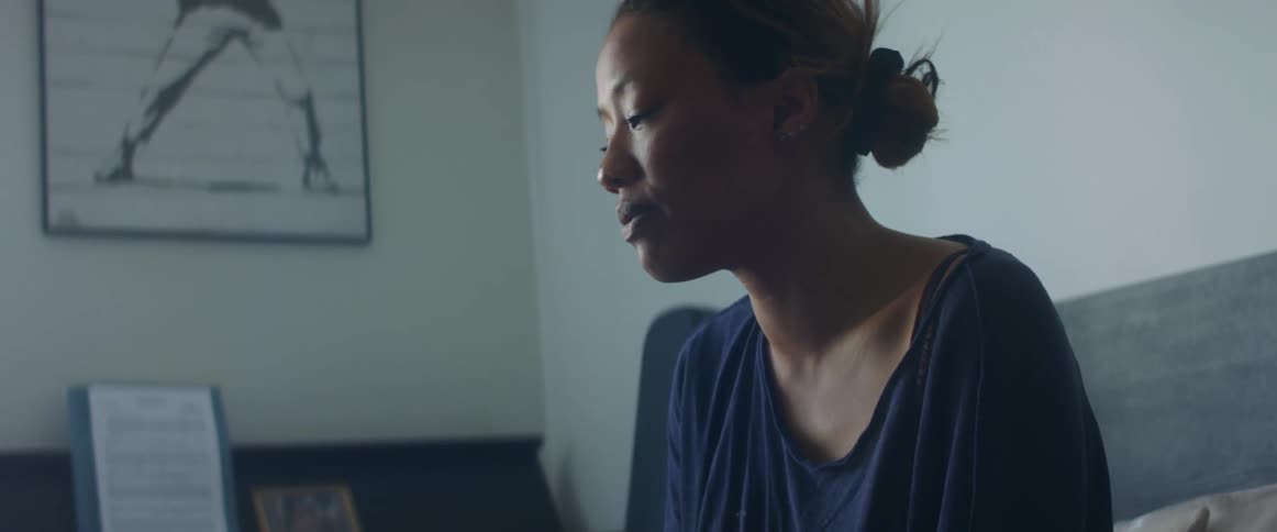 A woman sits on a couch looking at her cell phone with a sad look on her face