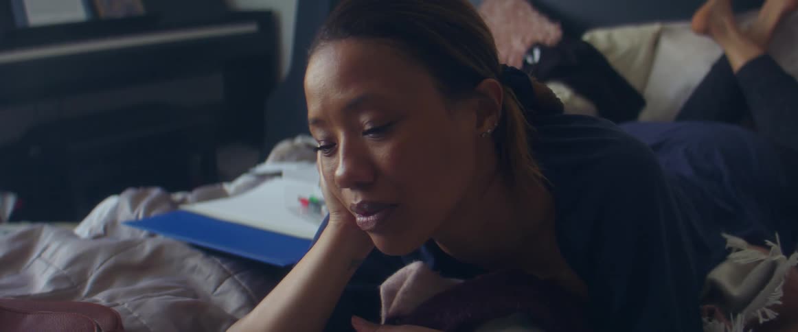 Woman lies on bed on her stomach watching laptop