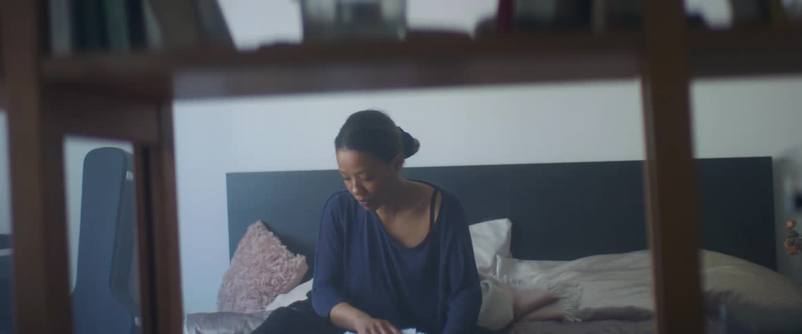 A woman in a bedroom sitting in bed holding a stack of papers with a wall in the background