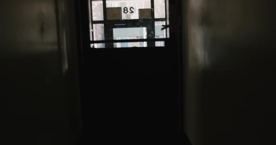 A person carrying clothing covered in plastic over their shoulder exits an apartment building