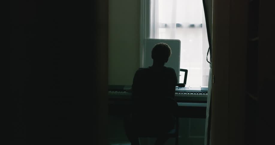 The silhouette of a person can be seen as they sit in front of a large keyboard