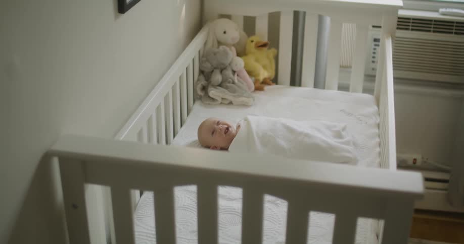 Baby lying on back in crib in room cooled by wind ac unit yawns and moves around