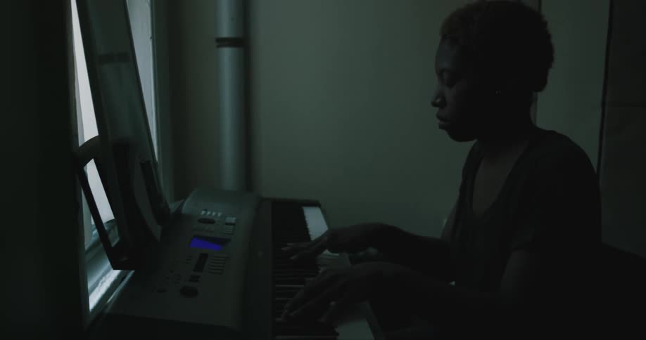 Silhouette of a person playing a keyboard inside a dimly lit room
