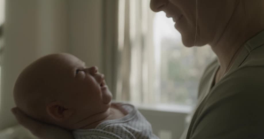 A woman cradles her babys head as she holds and kisses him