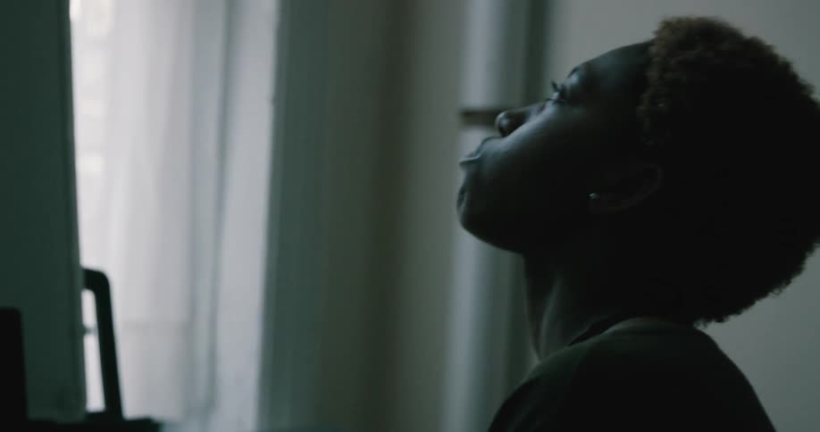 A woman sits alone in a room and looks up at the ceiling as she is contemplating something
