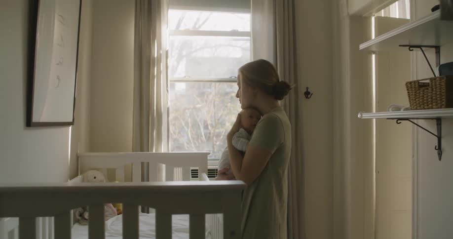 Mother hugs newborn baby next to the crib inside a room at home