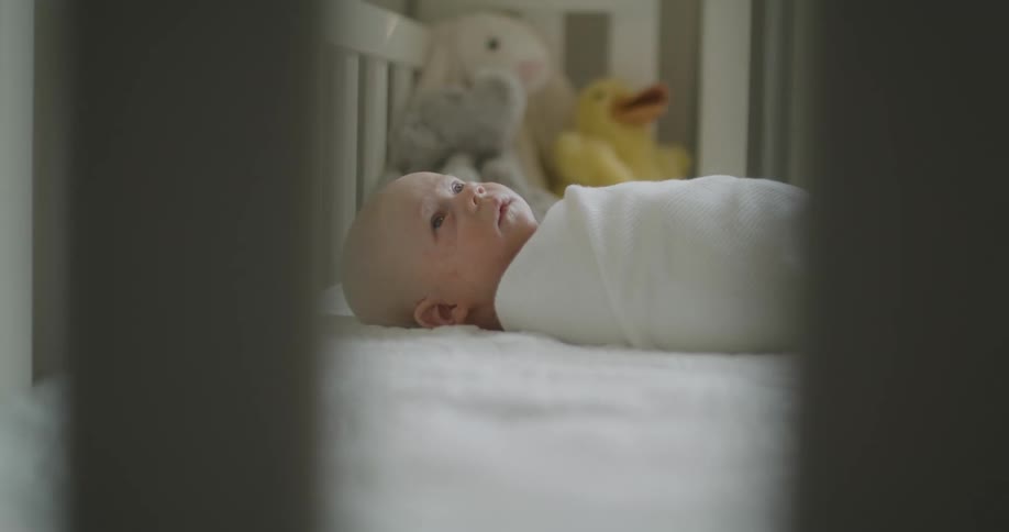 Newborn baby wrapped in a white blanket laying in a crib