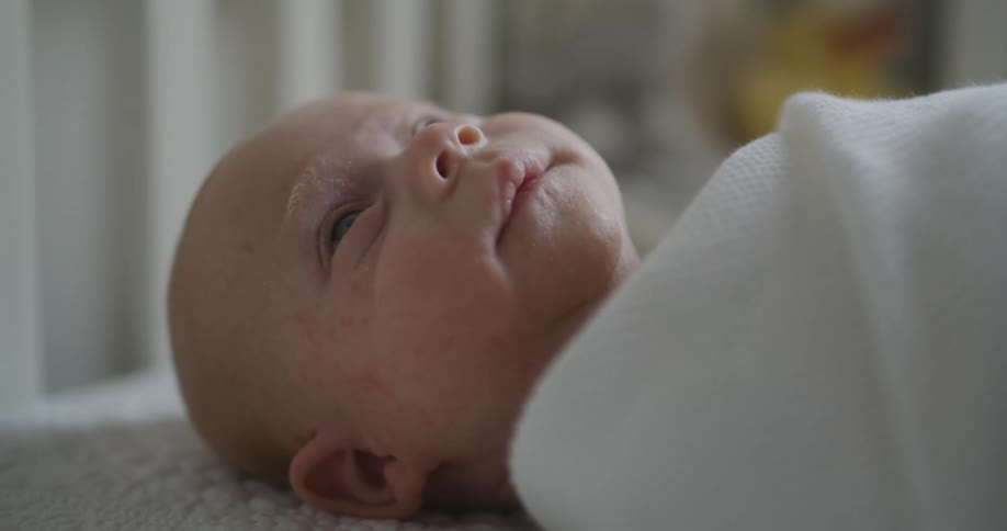 A baby rests in a crib while wrapped in a blanket