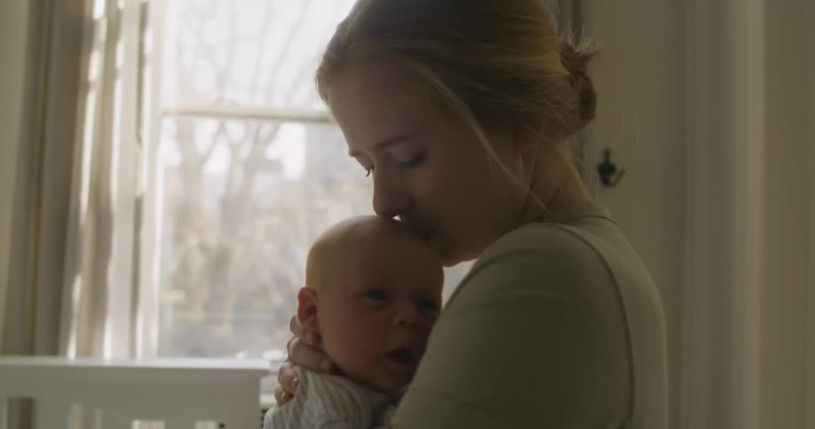 A woman kisses the head of an infant while rocking the infant in her arms
