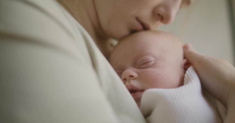 A woman holding a baby in a room wrapped in a blanket with a wall in the background