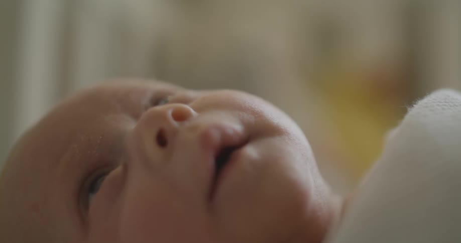 A newborn lying down covered by a blanket yawns big