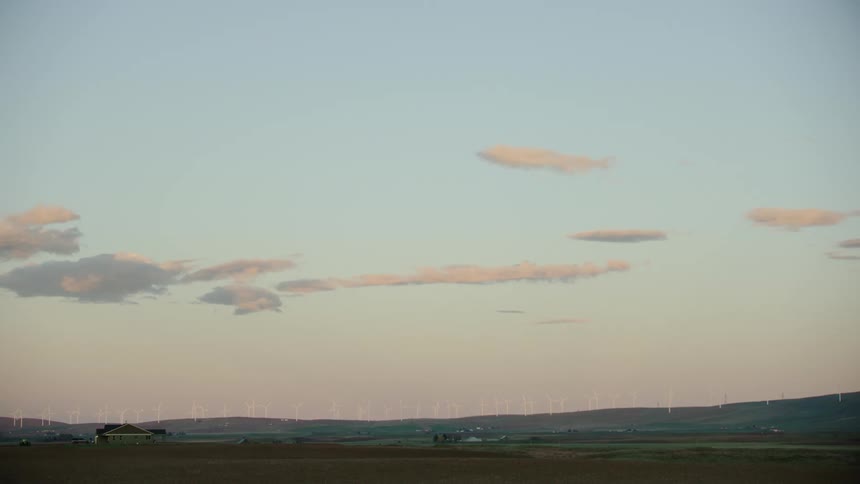 Windmills generate clean and renewable energy on a far away ridge as white puffy clouds hang in the sky just as the sun is setting