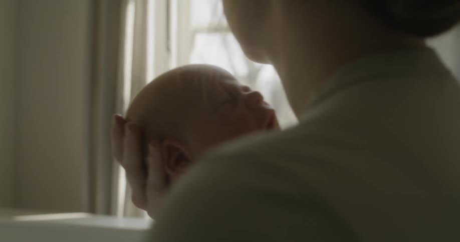 A woman holding a baby in a bedroom with a wall and window in the background