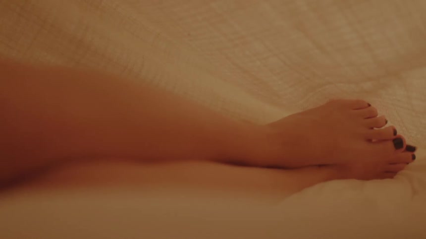 A woman laying in bed under the sheets rubs her feets together