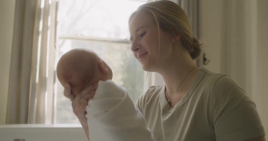 Mother picks up a baby from a crib in a room at home