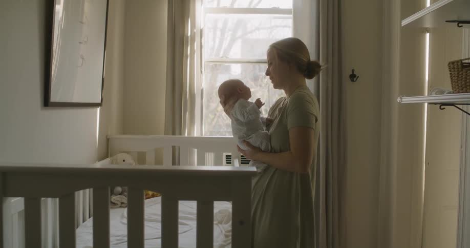 A young woman lifts her small baby out of its crib and gently cradles it in her arms
