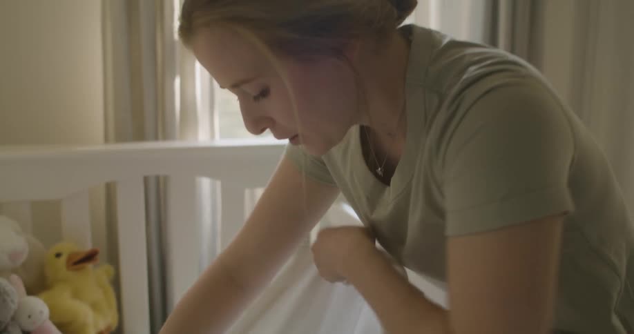 A woman places an infant in a crib and wraps the infant in a blanket