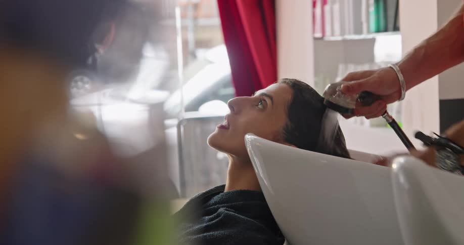 A woman in a hair salon getting her hair washed with a hose with water