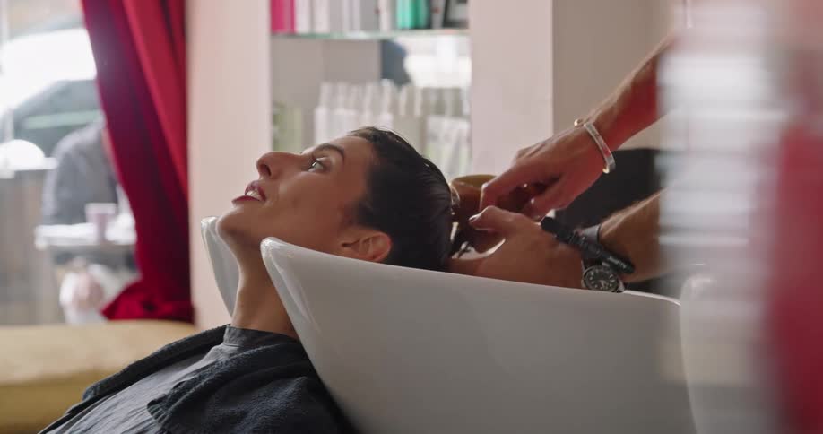 A woman talks and laughs while having her hair washed and brushed by a hairdresser in a salon