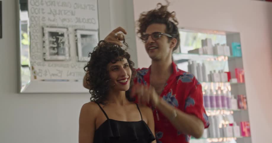 Male hair stylists adjusts womans curls as they talk