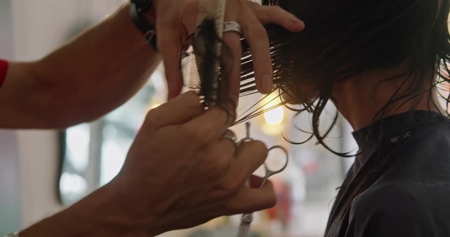 A hairdresser uses a comb and scissors to section and cut a clients wet hair