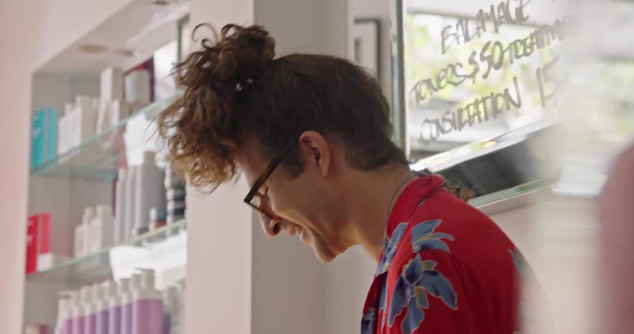 A man with glasses in a hair salon with a wall and a mirror in the background