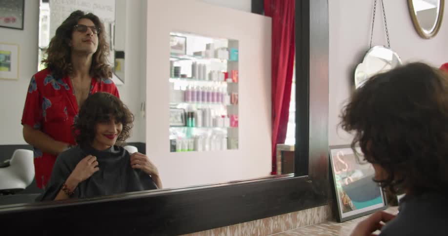 A male hairstylist drapes a cover over his customer before cutting her hair