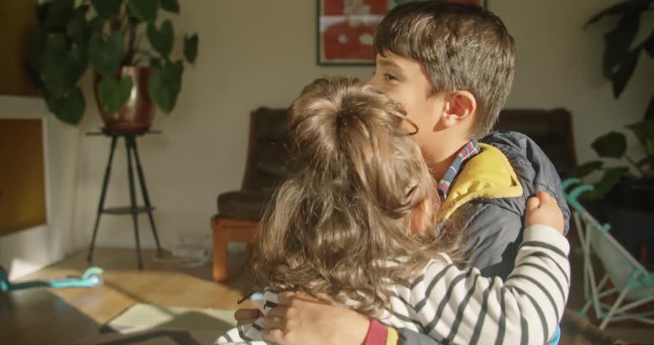 A boy and a girl in a room hugging with a couch and a wall in the background