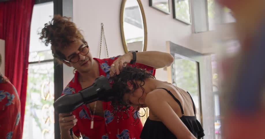 A man with glasses in a hair salon fixing a womans hair with a wall in the background