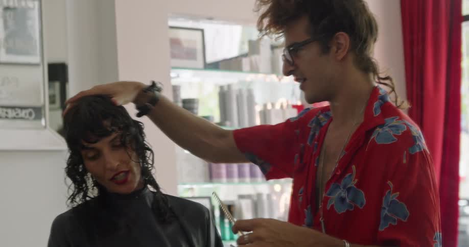 Male hairstylist wearing hawaiian shirt talks to customer while he cuts her hair
