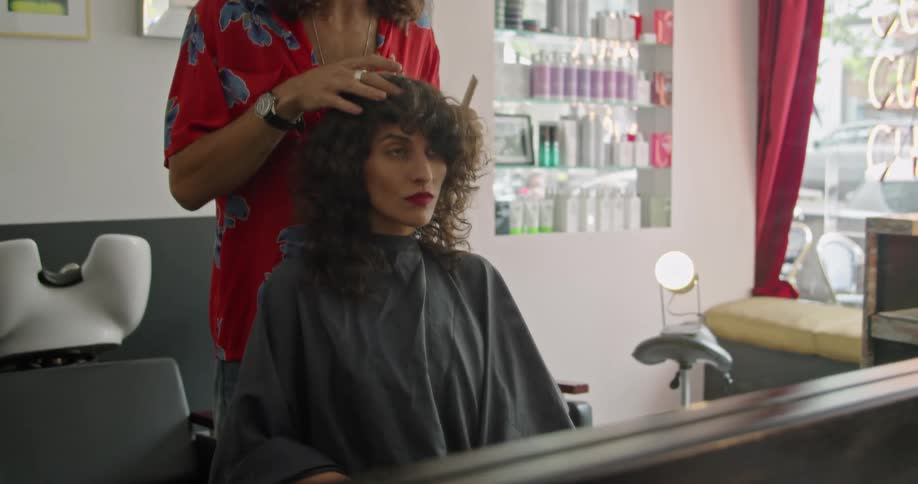 A male hairstylist teases at the curls of a female customer as he styles her hair