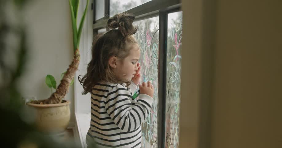 A young girl takes a marker and begins drawing a circle on a glass window