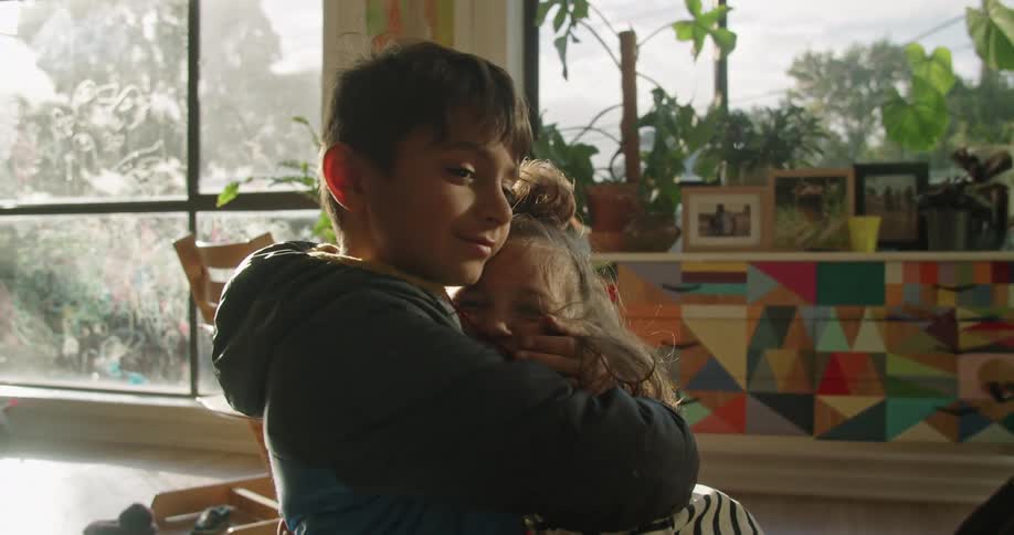A boy and a girl in a room hugging with plants and picture frames in the background