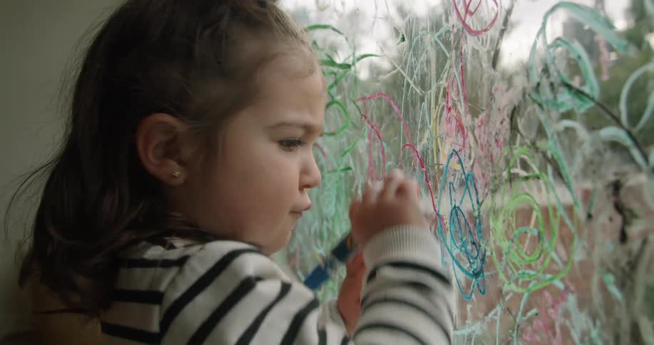 A young girl concentrates as she draws circles on a glass window with marker
