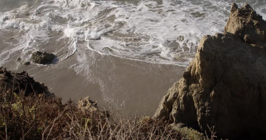 White foamy waves roll onto the beach near some rocks