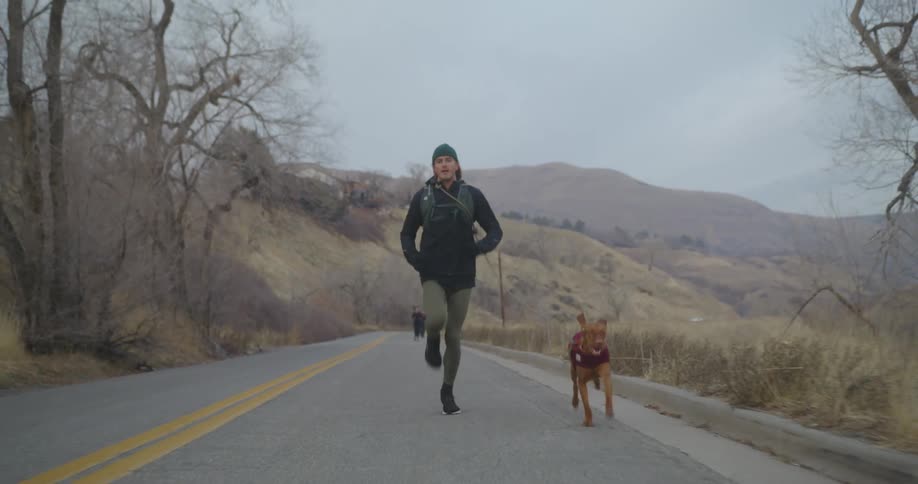 A tall man runs swiftly along a remote road along with his dog