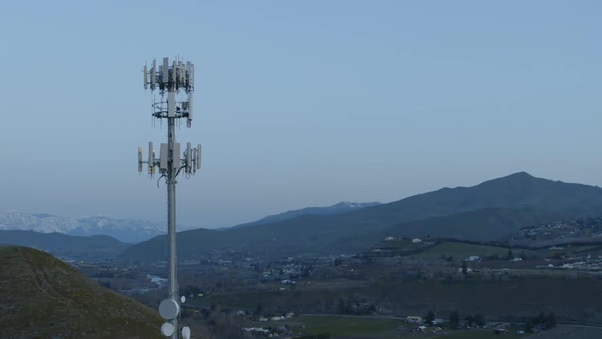A cell tower stands tall above a valley and mountain community below