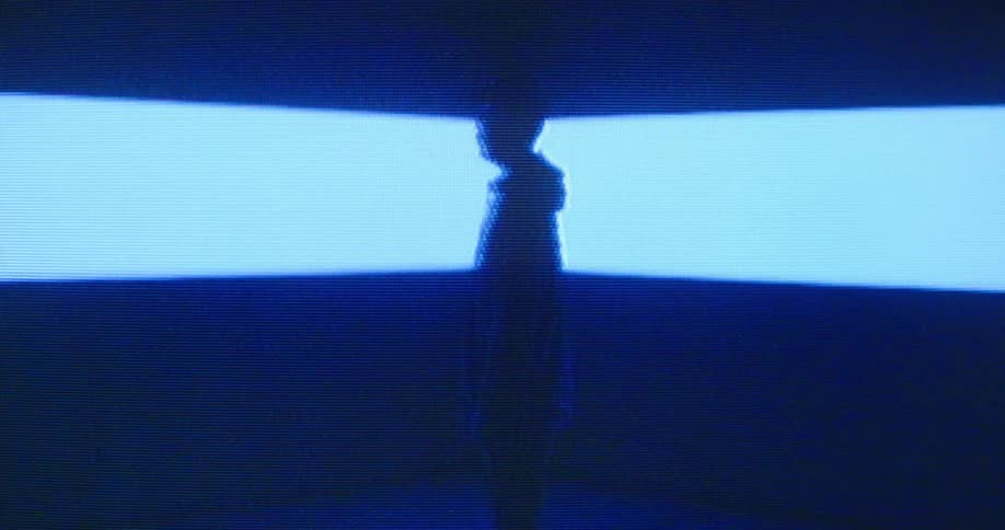 The silhouette of a man is seen as he stands in front of a large digital screen flashing color
