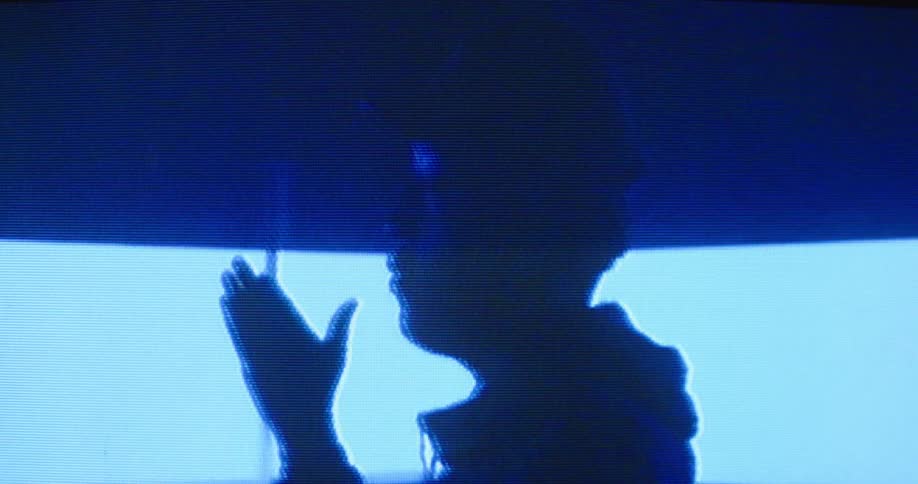 Distorted and static filled footage turns clear and shows a man in profile twirling a drumstick in his fingers