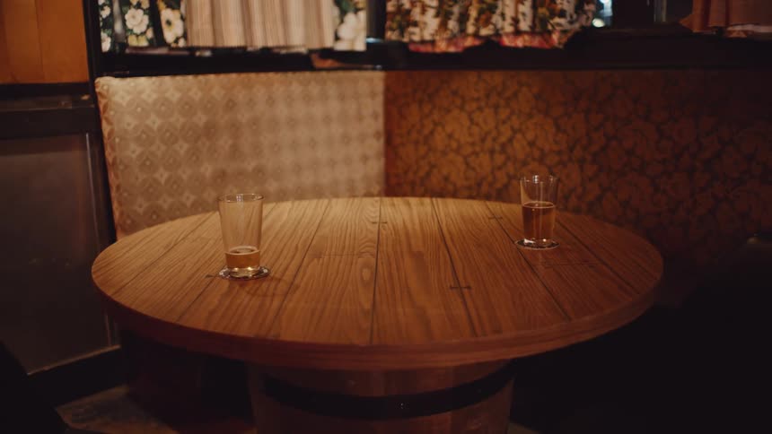 Two beers sit on wooden table with pedestal made of beer kegs in corner booth near window