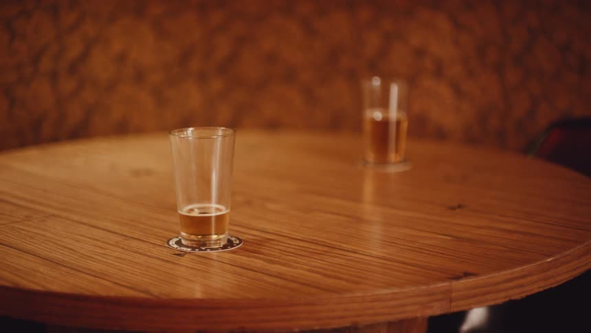 Two beer glasses on wood round table close to the brown wall