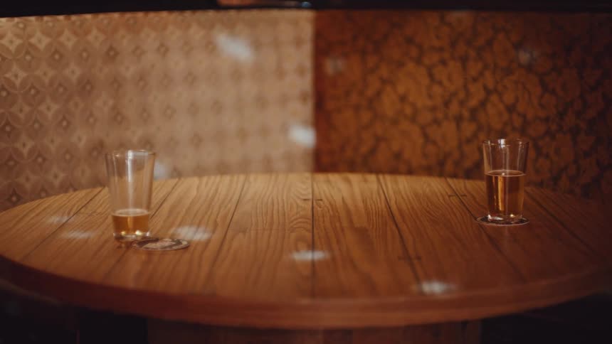 Two glasses of beer sit on wooden table in booth as white lights dance across