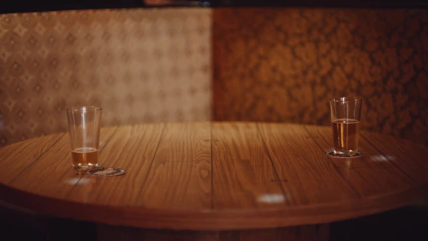 A room with two glasses on a table with coasters with a wall in the background