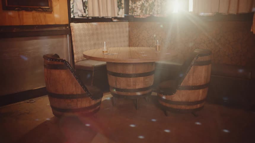 Two glasses of beer sit on table in booth with chairs shaped like beer kegs as lights dance around