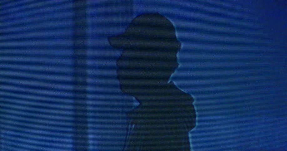 The silhouette of a man standing in profile as lights words and static flash around him and blur