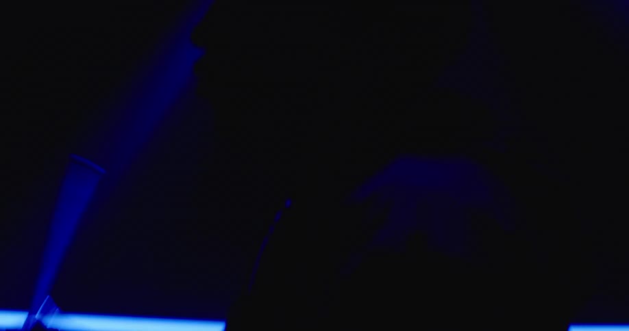 The silhouette of a musician holding and twirling a drumstick as blue light and shadow surround him